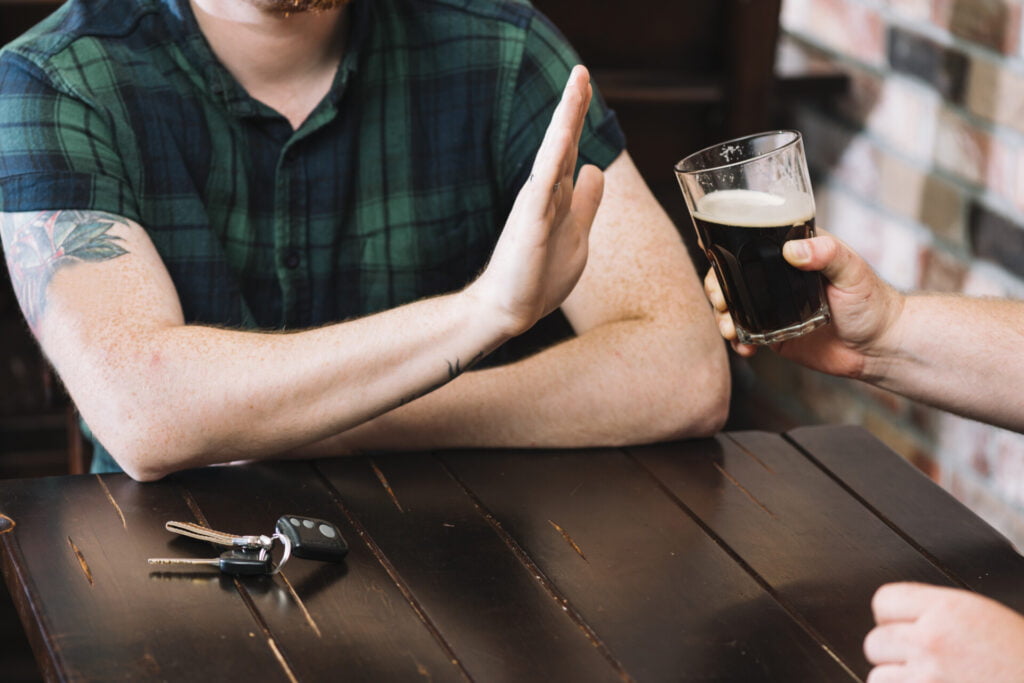 Persona rechaza un vaso de alcohol con su mano.