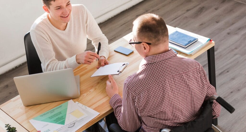 Gestor de inclusión Laboral junto a personas con discapacidad frente a un escritorio conversando.