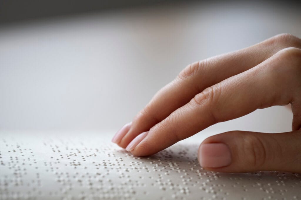 Imagen de un libro con texto en Braille y una mano tocando los puntos elevados.