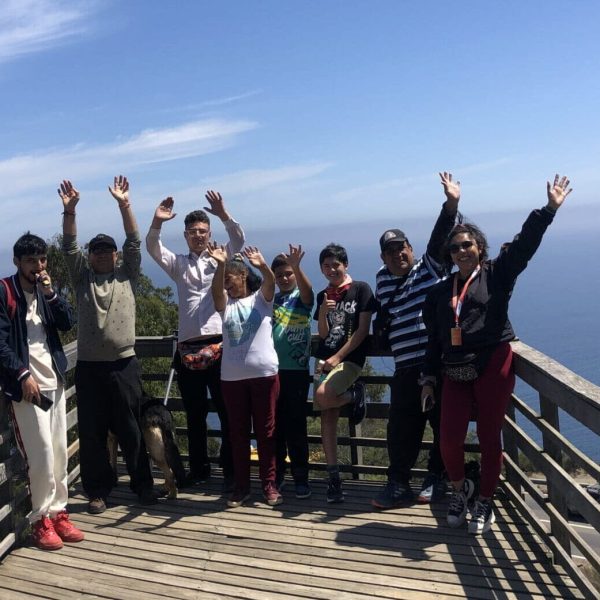 Programa PAI Grupo de personas celebrando con los brazos en alto mientras posan para la cámara, con el mar de fondo.